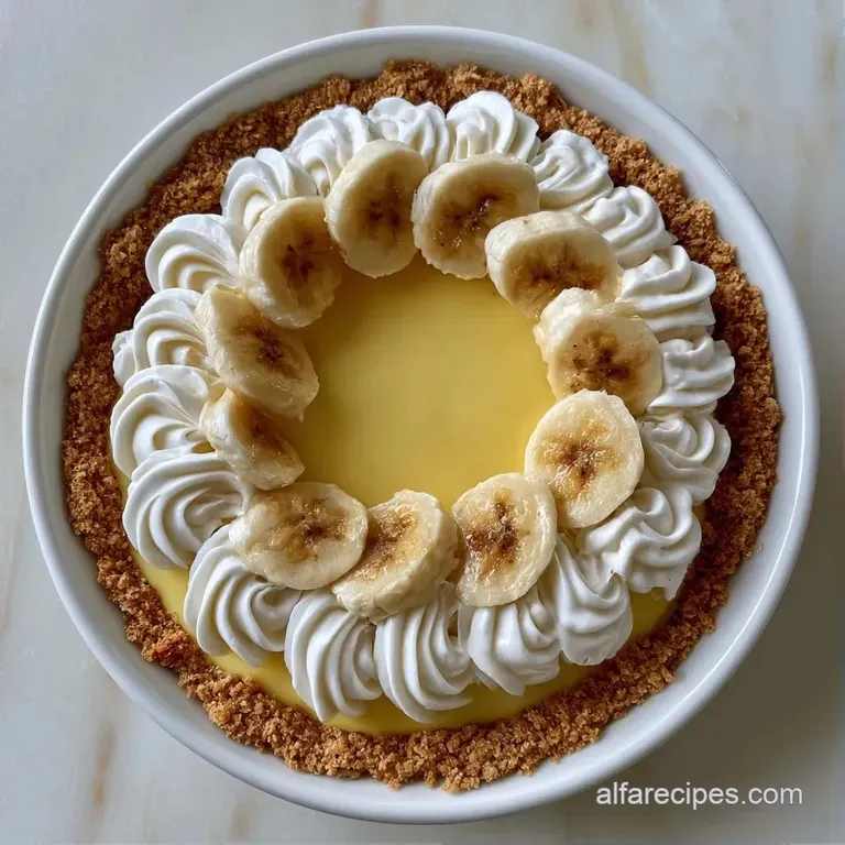 A slice of creamy custard pie with fluffy white peaks and fresh banana coins on a clean, modern white ceramic plate.