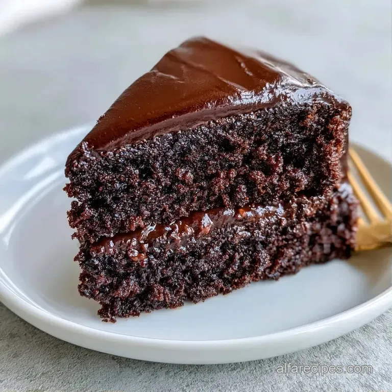A slice of moist dark chocolate cake on white porcelain, paired with a swirl of cream and a fresh mint leaf.