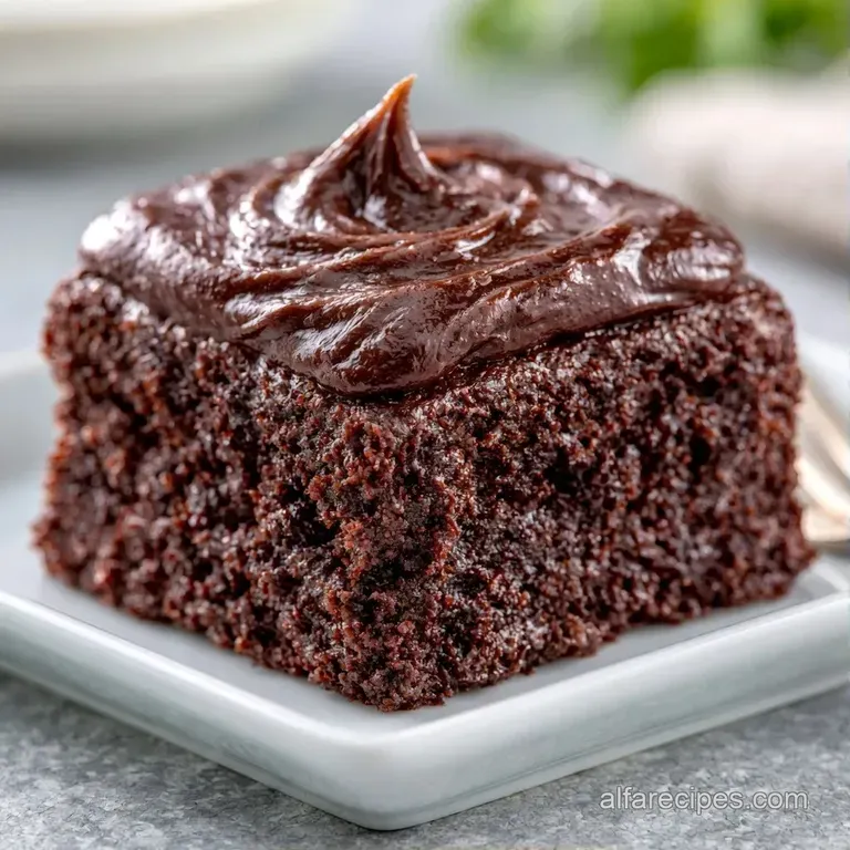 A neat square slice of dark chocolate cake on a white plate, garnished with a fresh raspberry and mint leaf.